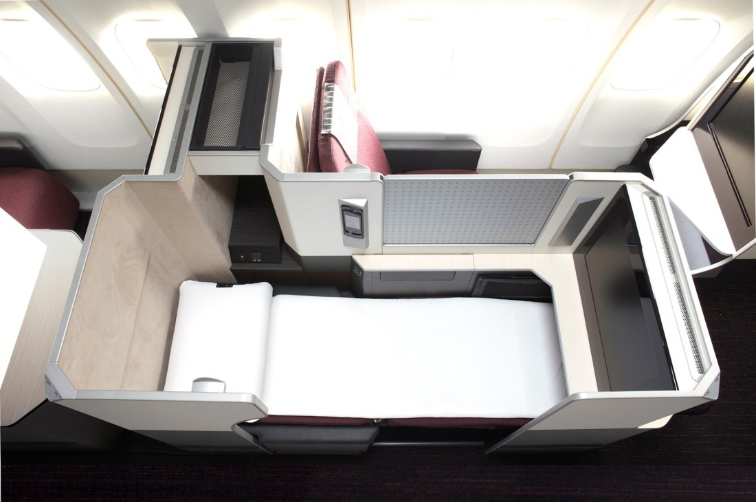 Overhead view of JAL aircraft first-class cabin with lie-flat bed and burgundy seating.