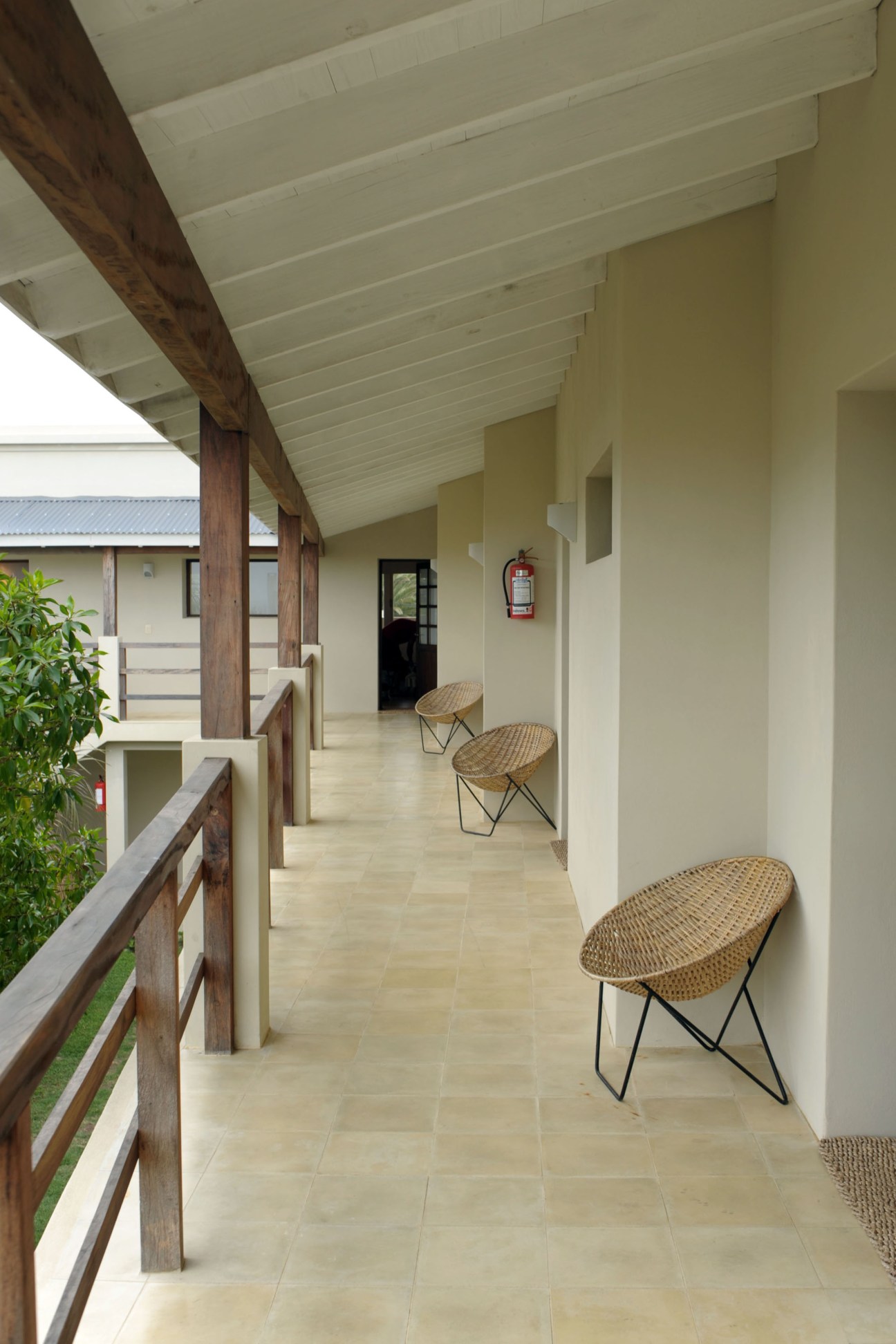 A covered porch at Brisas de la Pedrera hotel with woven chairs, white ceiling beams, and dark wooden railings.