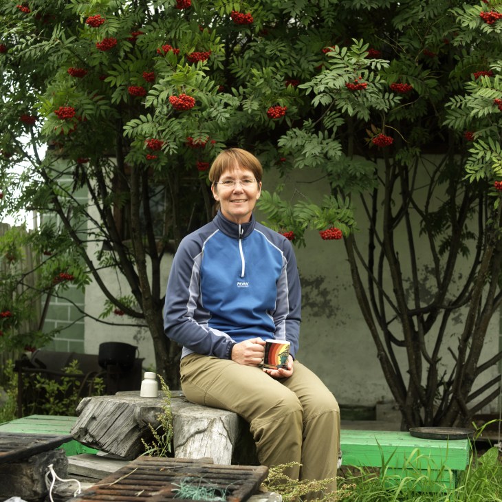 Martha Madsen sits outdoors holding a product, with red rowan berries hanging from branches behind her.