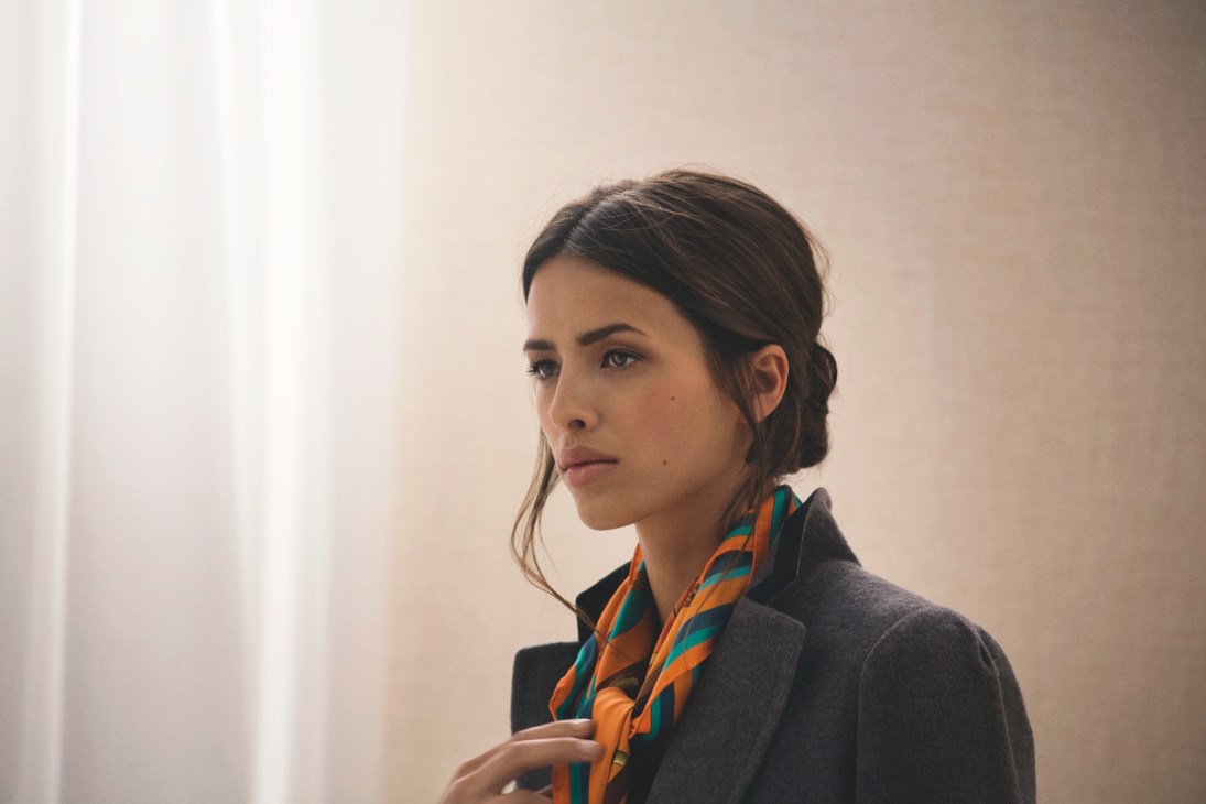 Woman wearing a dark jacket and colorful striped scarf by Hermès, photographed in profile against a neutral background.