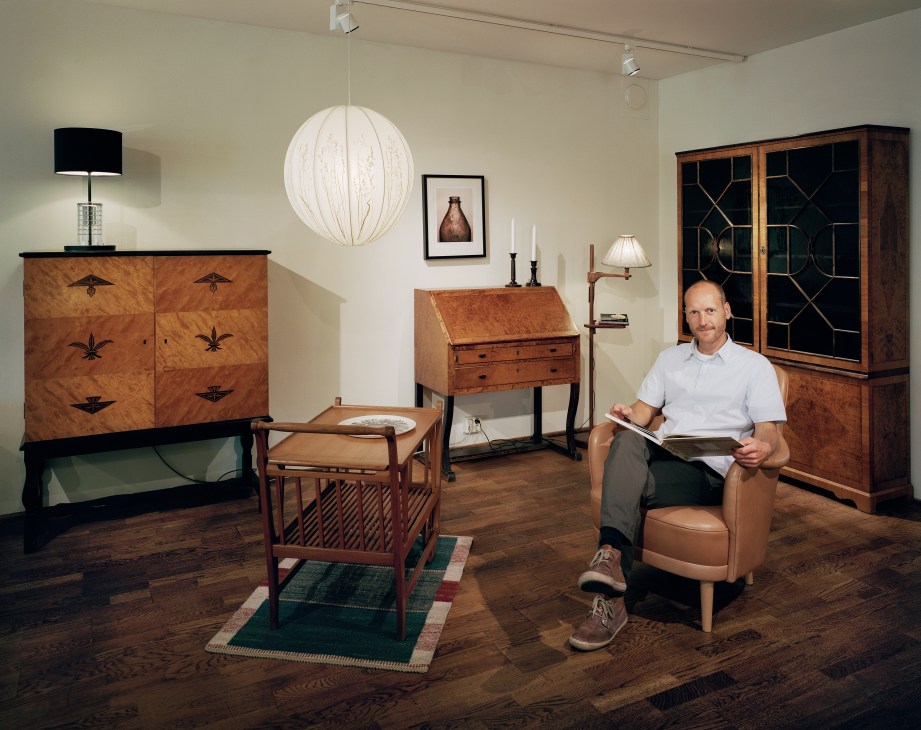 Jerk Malmsten sits in a tan leather armchair surrounded by vintage wooden furniture and lighting in the Carl Malmsten shop.