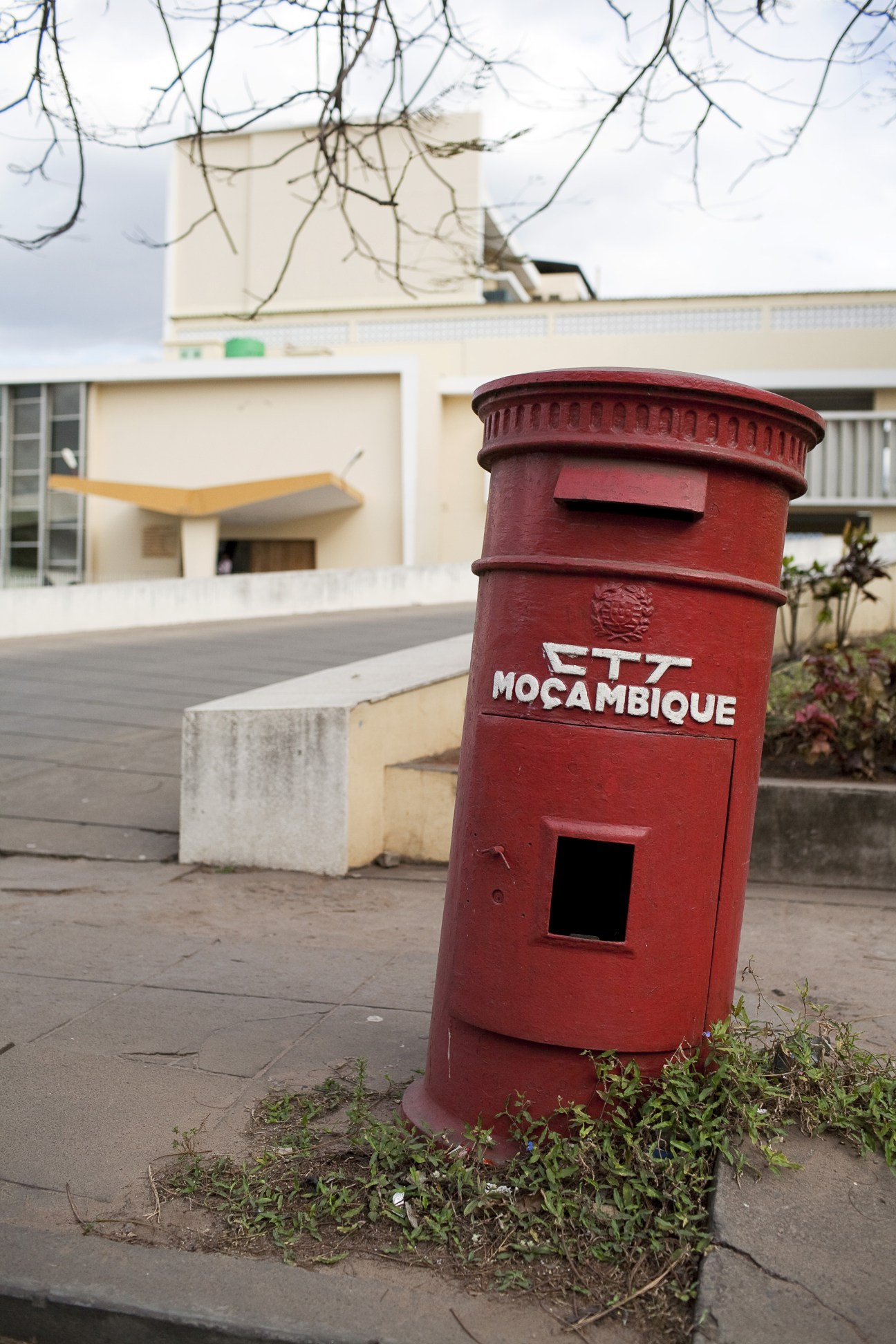 Red Portuguese colonial-style postbox labeled 'CTT MOÇAMBIQUE' on a city street.