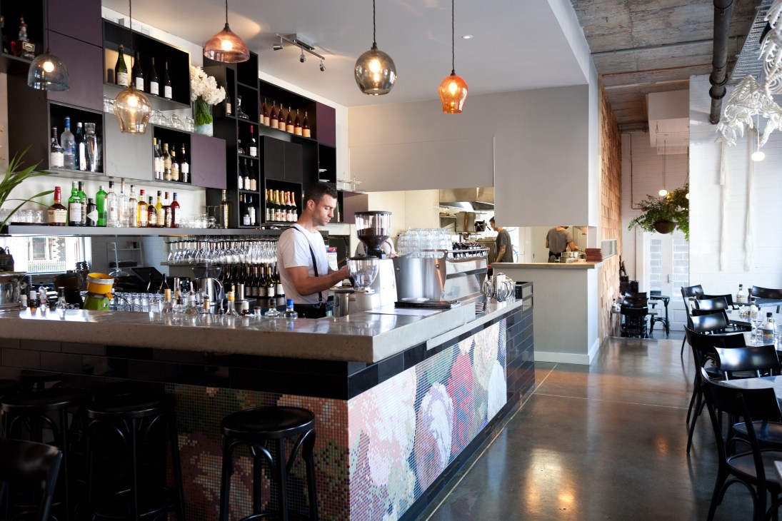 The Brix restaurant bar with pendant lights, shelving displaying bottles, and bartender serving drinks.