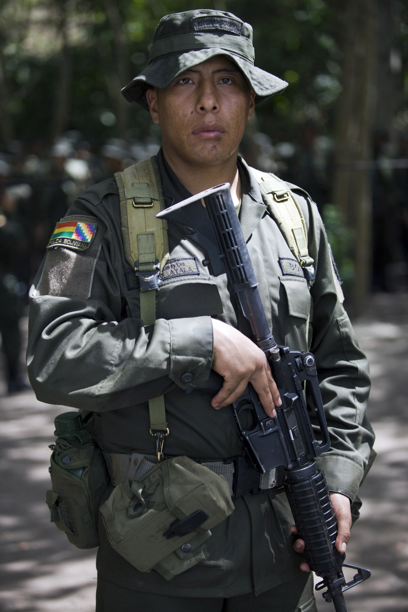 Bolivian police student in military uniform holding a rifle with tactical gear and Bolivia flag patch.