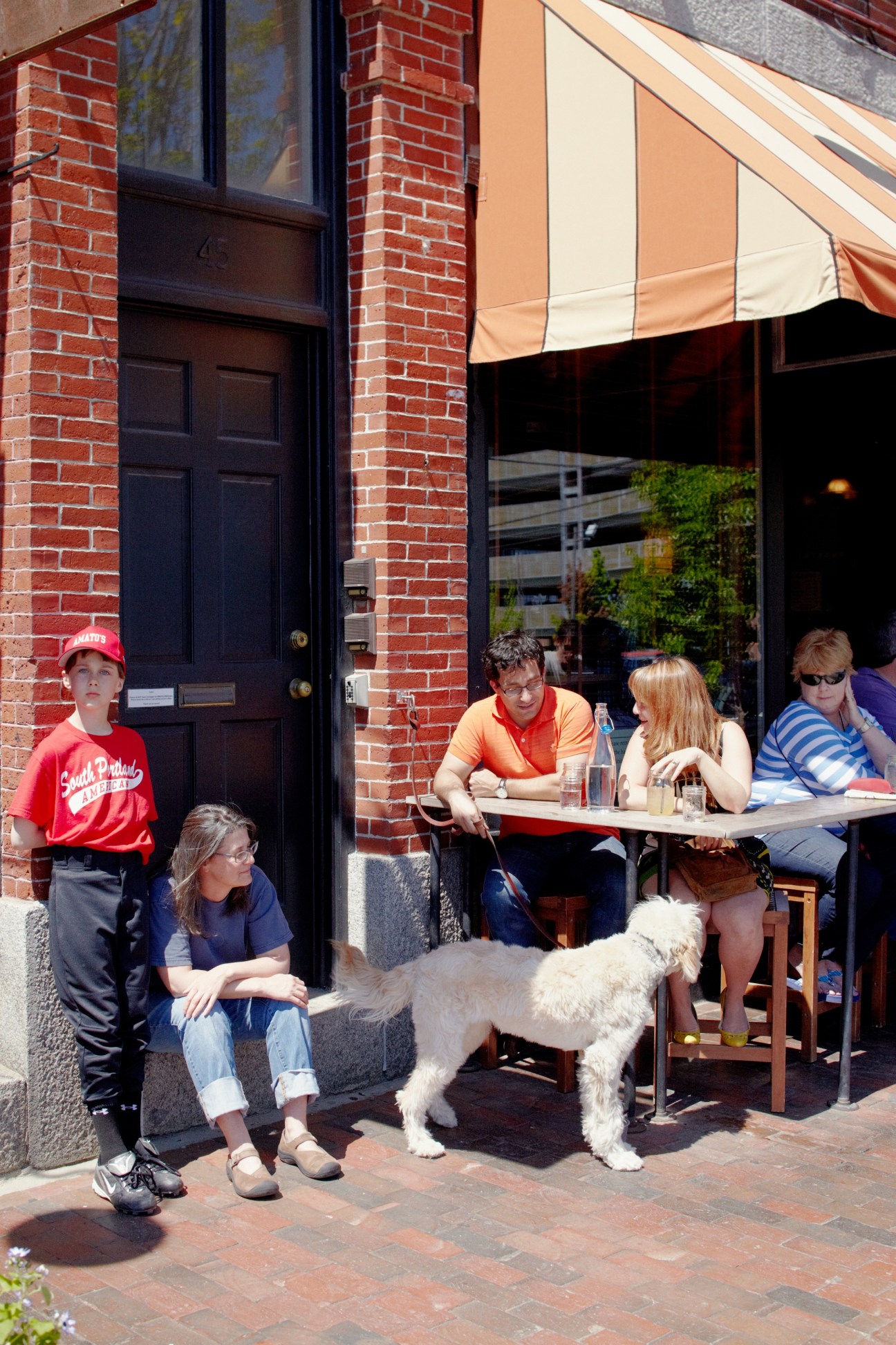 People and a dog sitting outside Duckfat restaurant on a brick sidewalk in Portland.