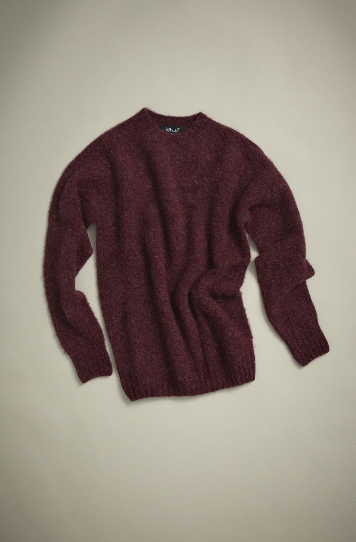 Deep burgundy knit sweater by Howlin' laid flat on neutral background.
