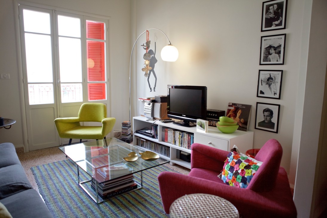 Modern living room with colorful mid-century furniture, glass coffee table, and framed black-and-white photographs on the wall.