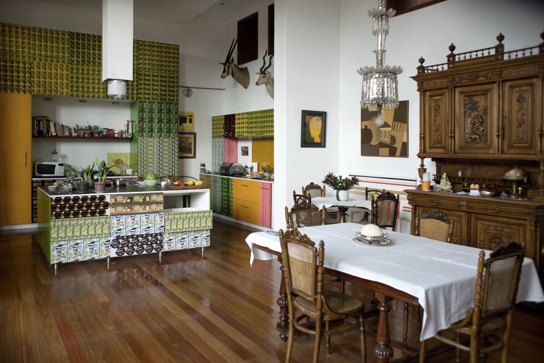 A renovated colonial kitchen and dining room with colorful patterned cabinetry, wooden furniture, and antique décor.