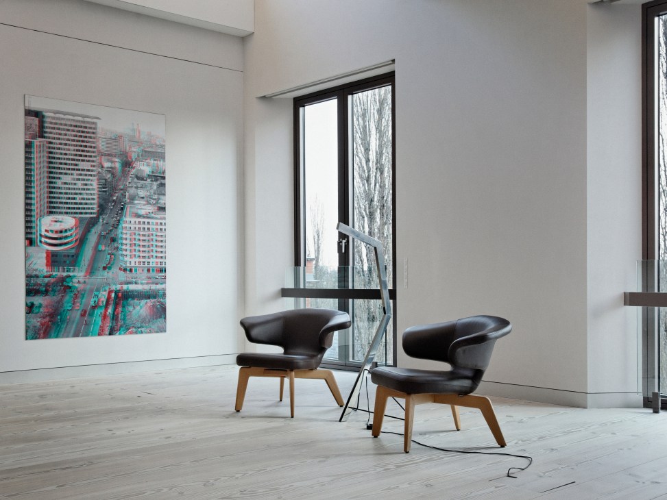 Modern minimalist entrance hall with two black leather chairs on wooden legs and large windows overlooking a city.