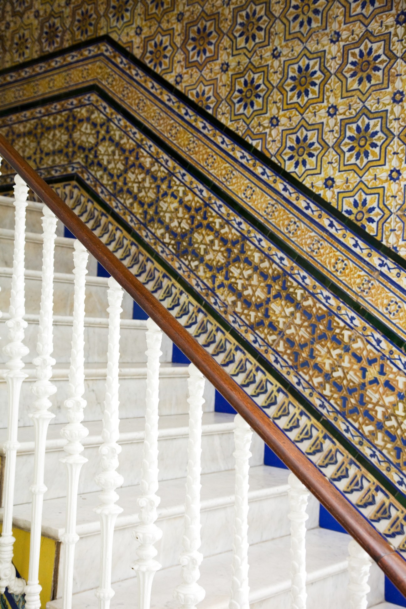 Ornate blue and gold patterned tilework on a staircase with white balustrade.