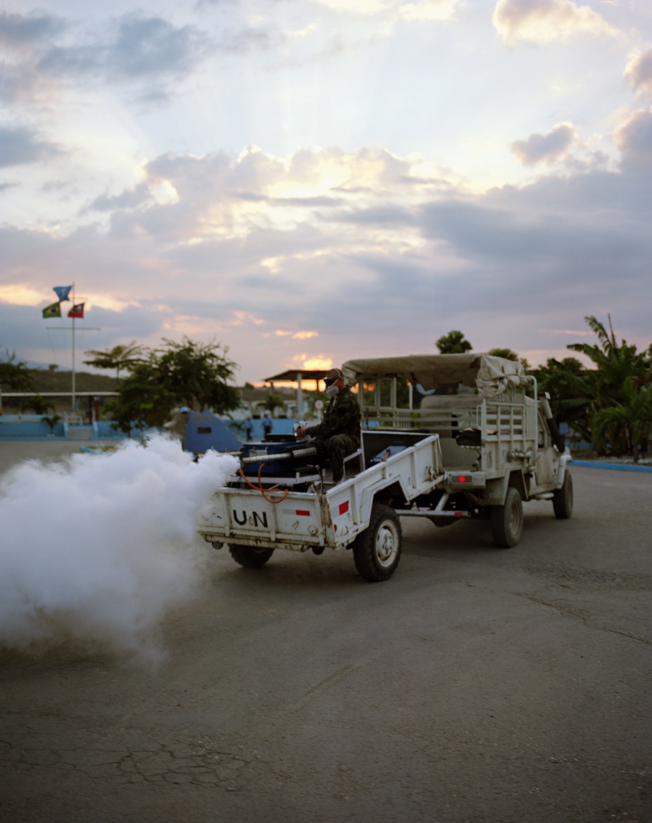 UN vehicles spraying insecticide at a military base in Haiti at dusk.