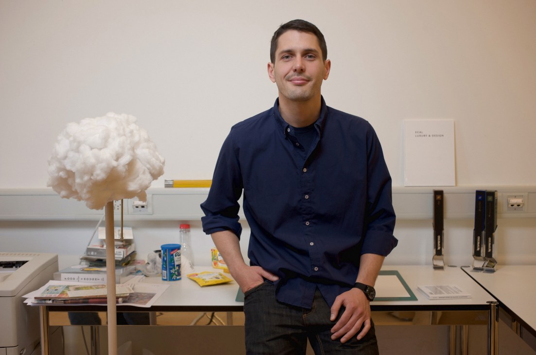 Augustin Scott de Martinville sits on a desk in an office with design sketches and a white sculptural model.
