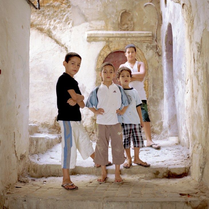 Children playing in a narrow, deteriorating alleyway with whitewashed walls in the Algiers casbah.