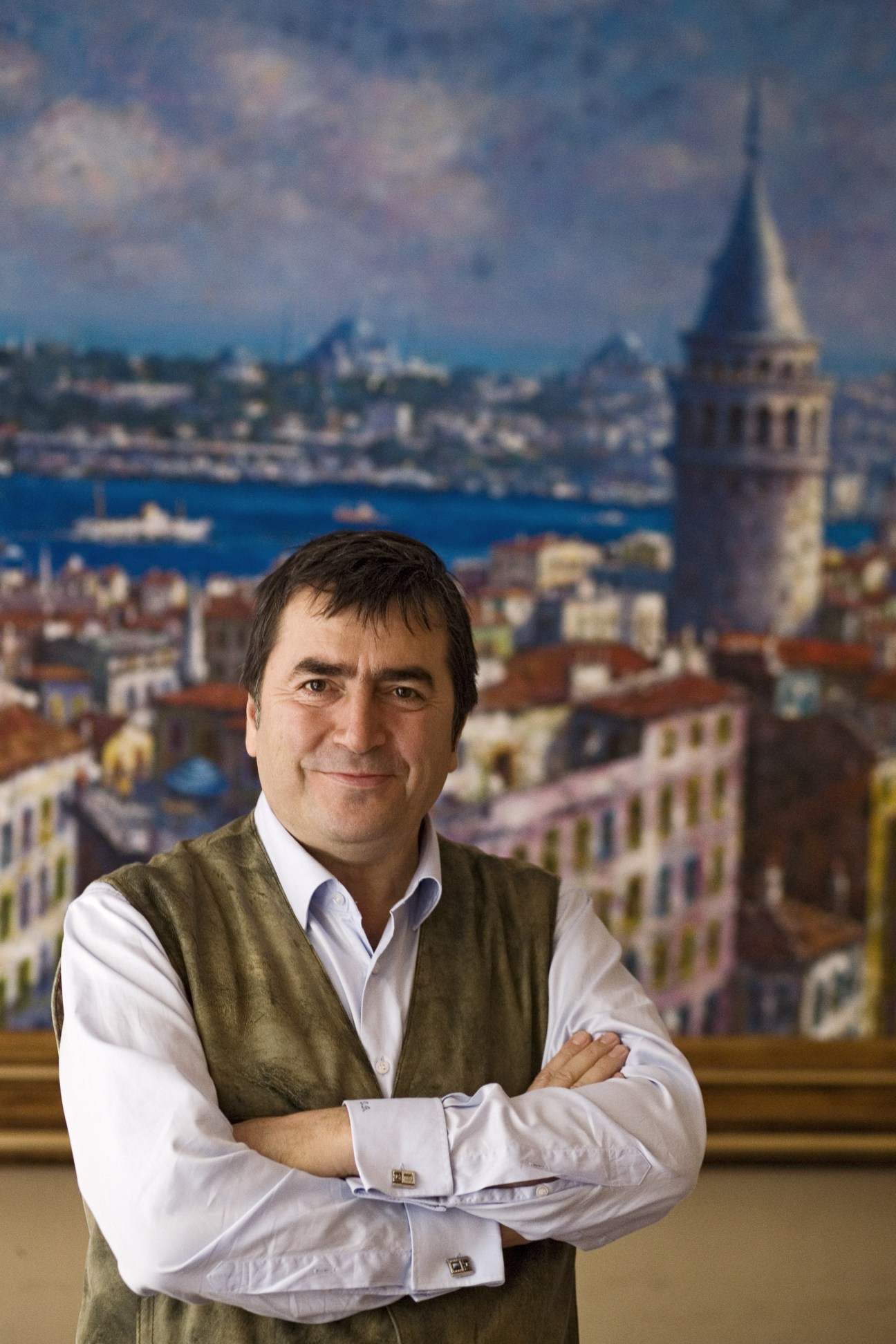 Ugur Bekdemir, owner of Asmalimescit Art Gallery, standing with arms crossed before an Istanbul cityscape backdrop featuring the Galata Tower.