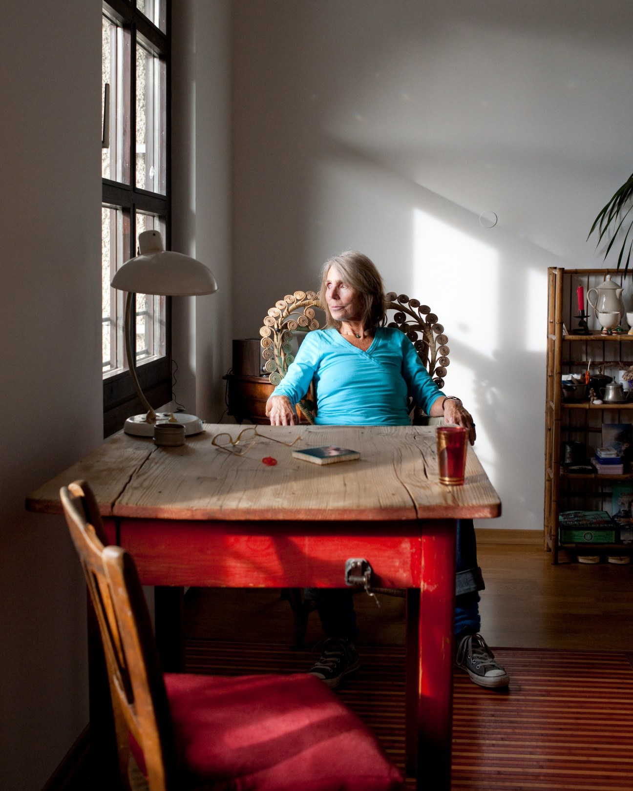 Actress Waki Meier sits at a red desk in her Munich apartment, wearing a blue top.