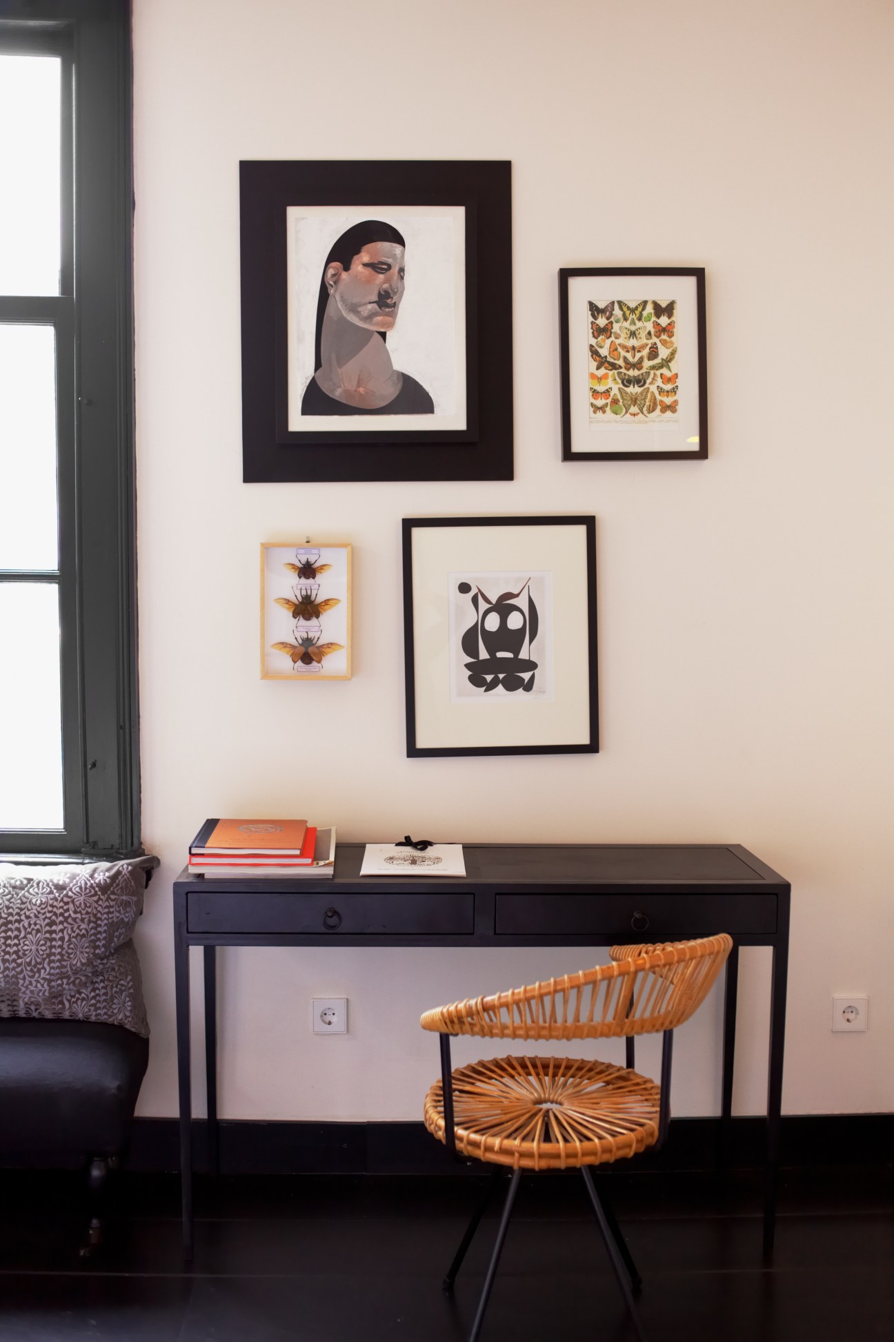 Interior workspace with framed artworks on wall and woven chair at black desk.