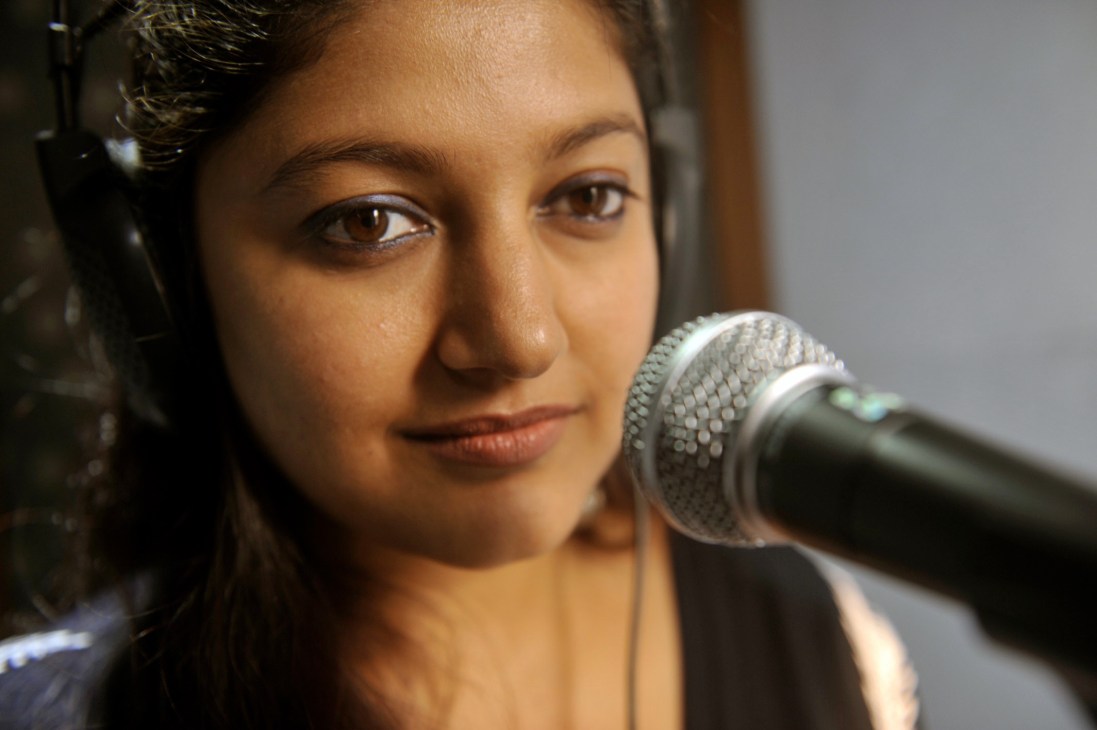 Mona Shetty, the Hindi voice of Angelina Jolie, speaking into a microphone while wearing headphones in a recording studio.