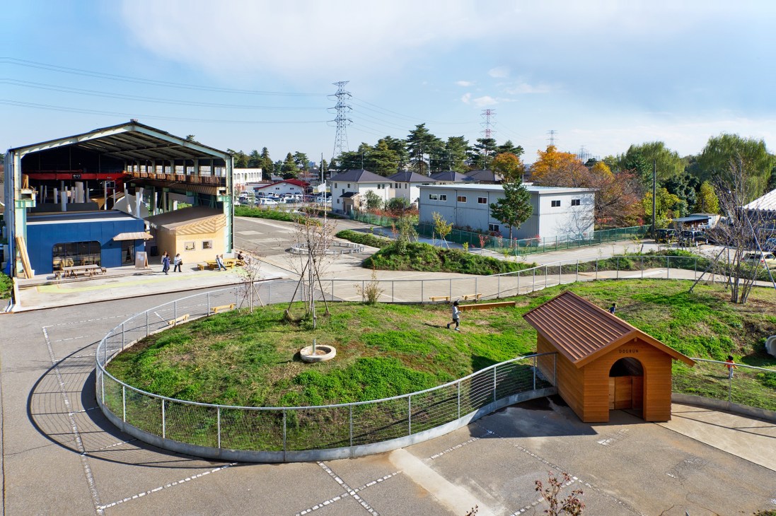 Aerial view of Newland community development in Kumagaya showing dog run with wooden kennel, landscaped grounds, and converted industrial buildings.