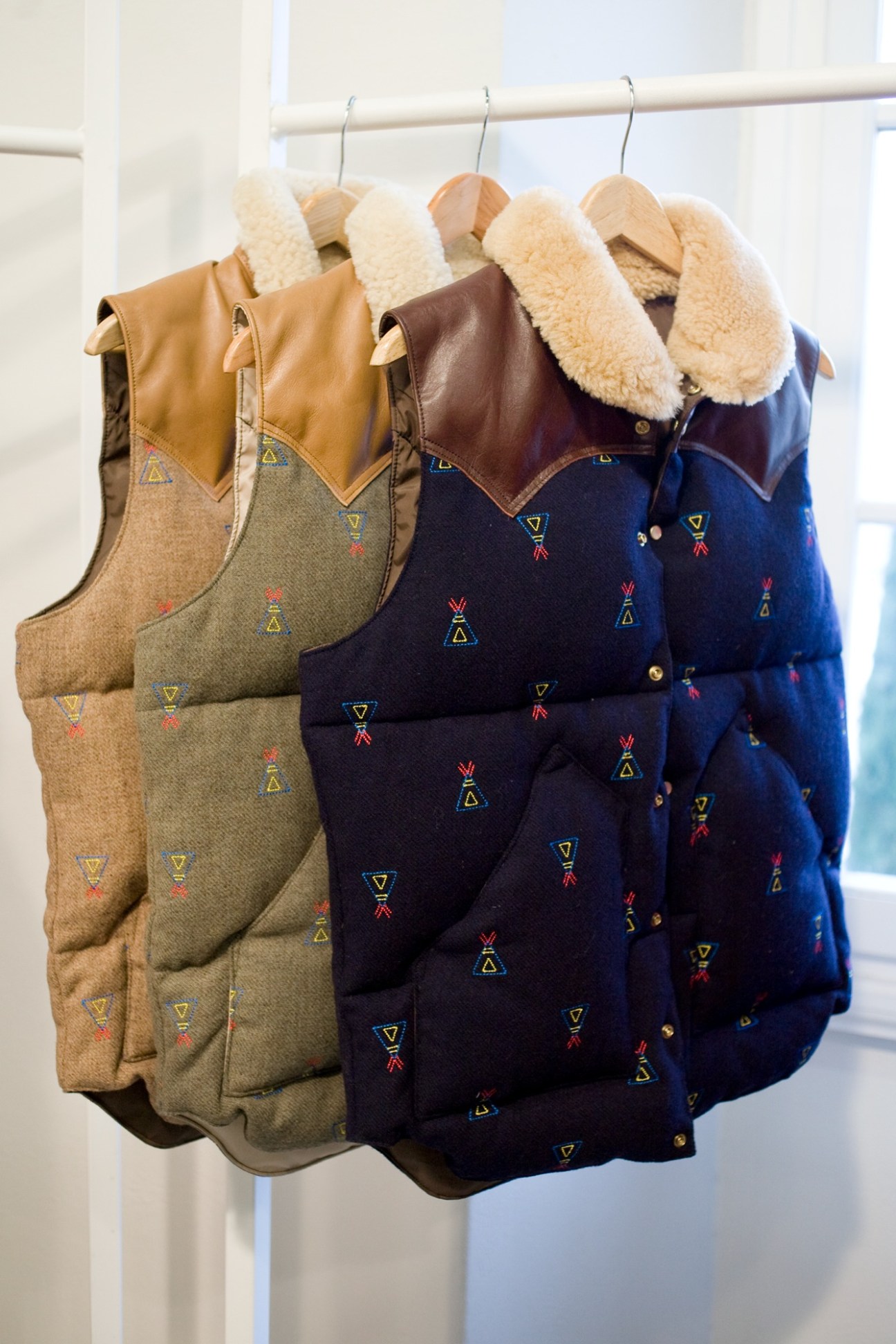 Rocky Mountain Featherbed padded vests in various colors hanging on wooden hangers with sheepskin collars.