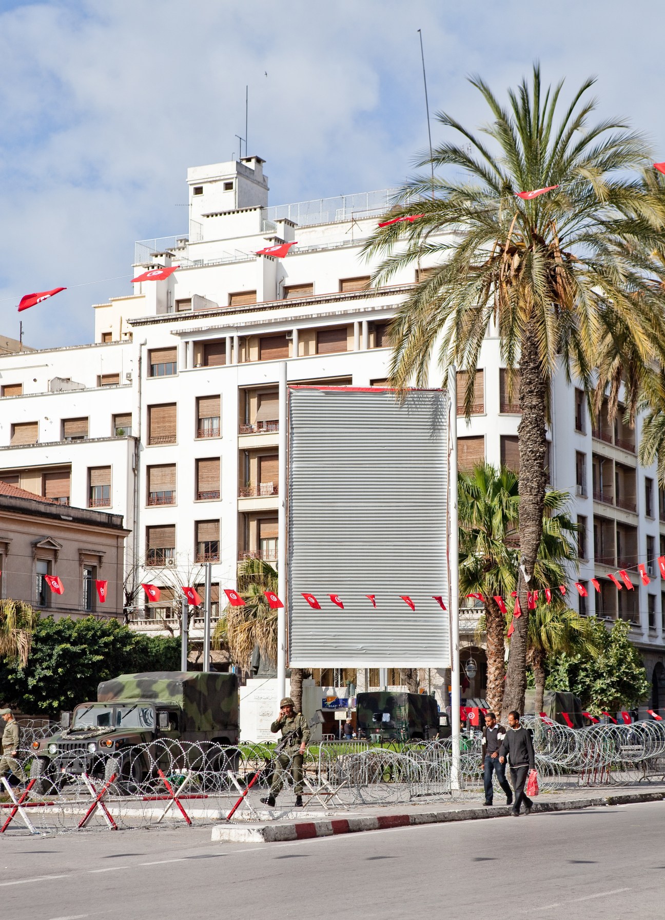 Empty billboard with metal corrugated shutter in Tunis surrounded by Tunisian flags and palm trees.