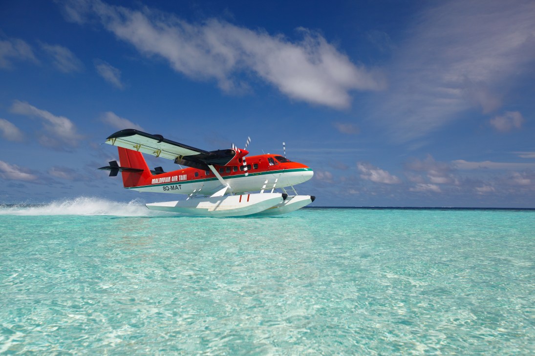 Red and white Maldivian Air Taxi seaplane moored in turquoise Maldivian waters.