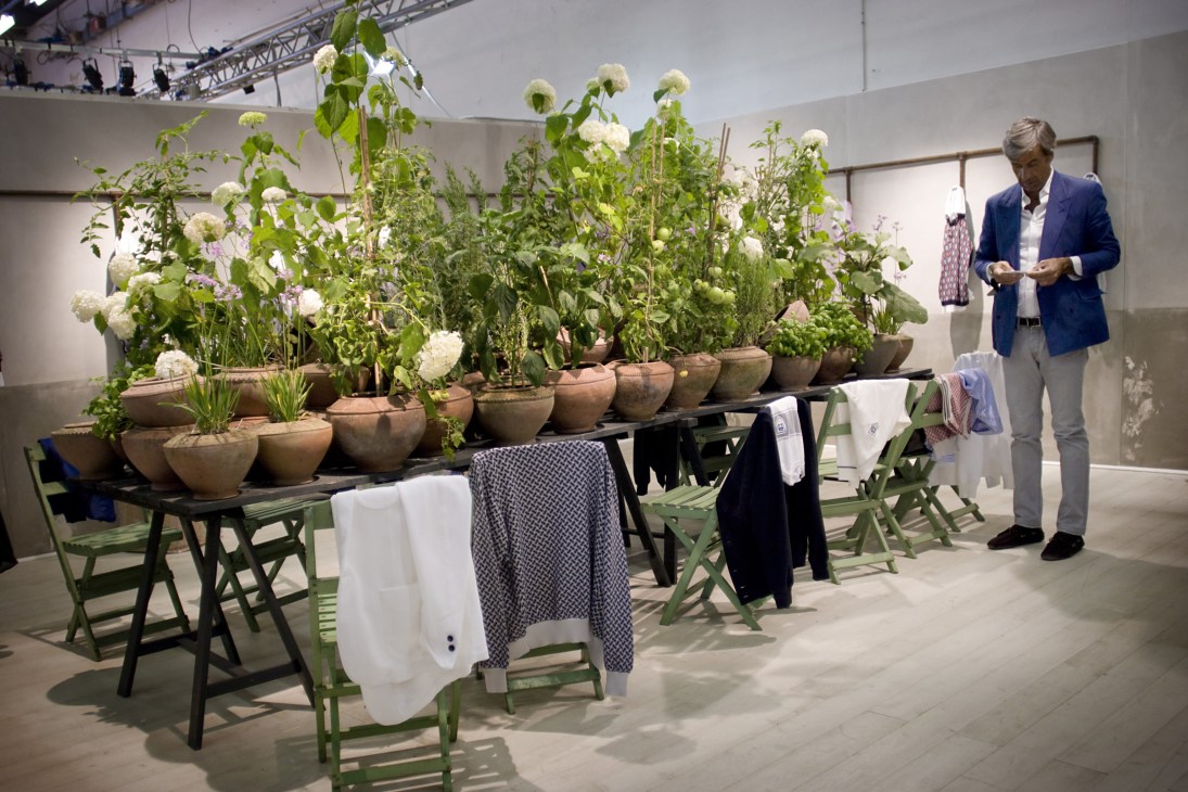 Man in blue blazer viewing Drumohr's exhibition stand decorated with potted plants and flowers, displaying knitwear samples.