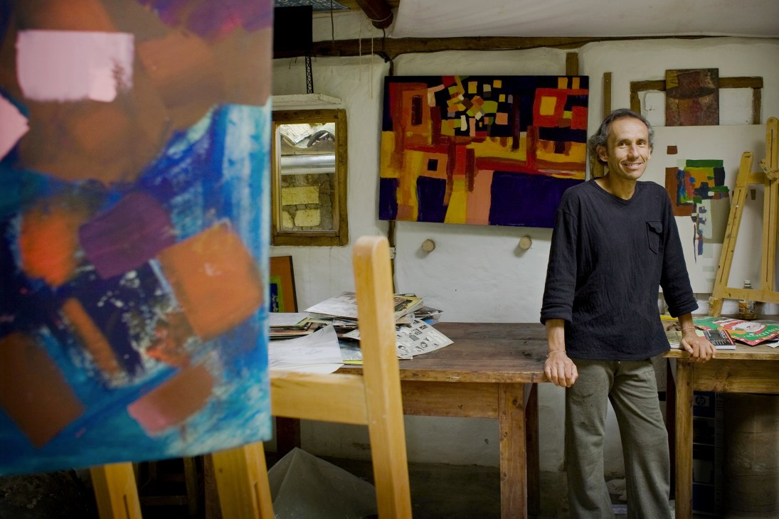 Architect Nestor Mesa stands in his studio surrounded by colorful abstract paintings and artwork.