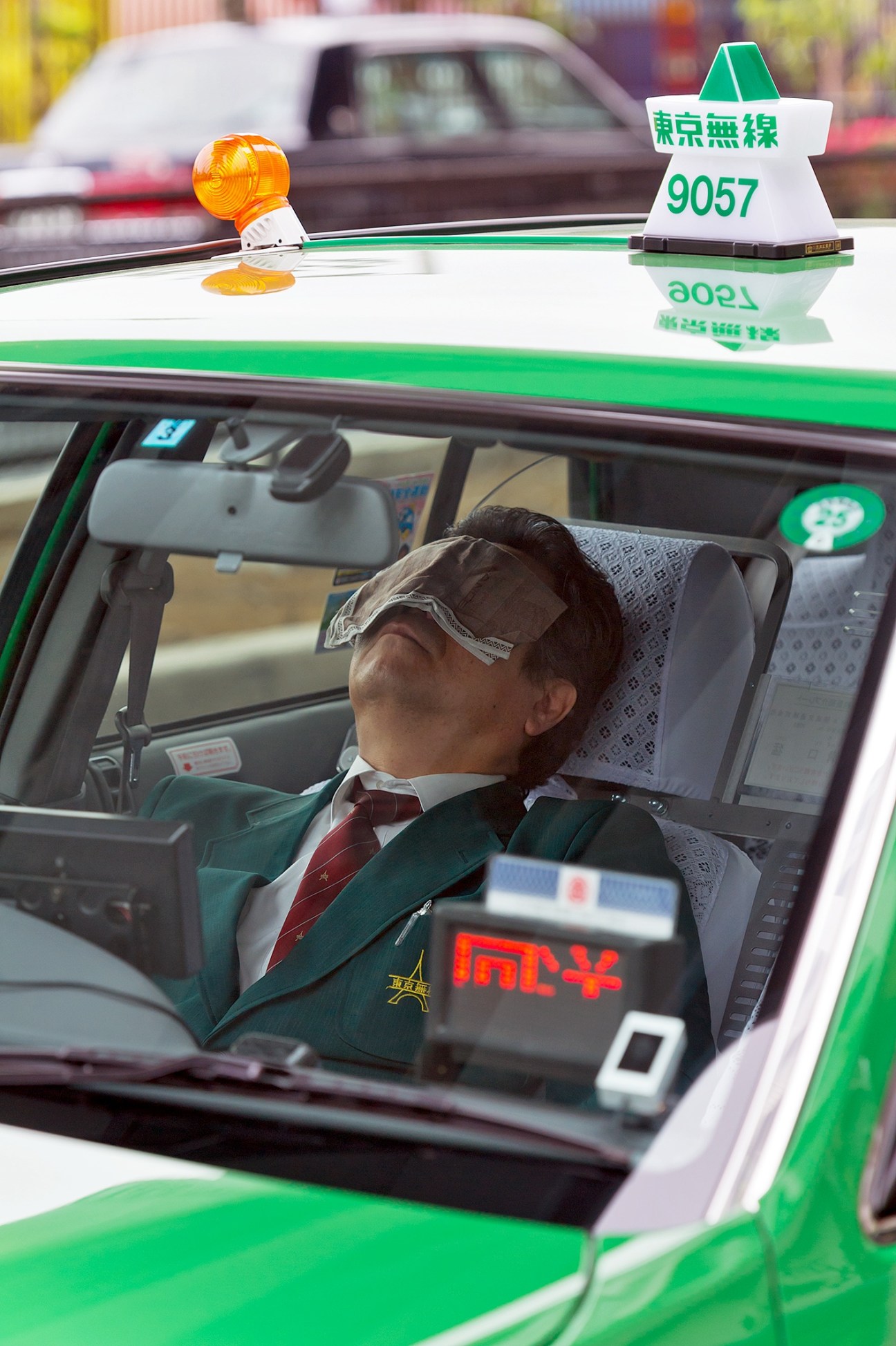 Tokyo taxi driver sleeping in his green and white Nihon Kotsu cab during a daytime rest break.