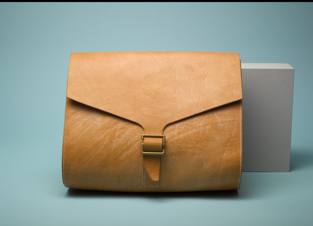 Tan leather hand-cut bag by Tender with brass buckle closure and stitched detail.