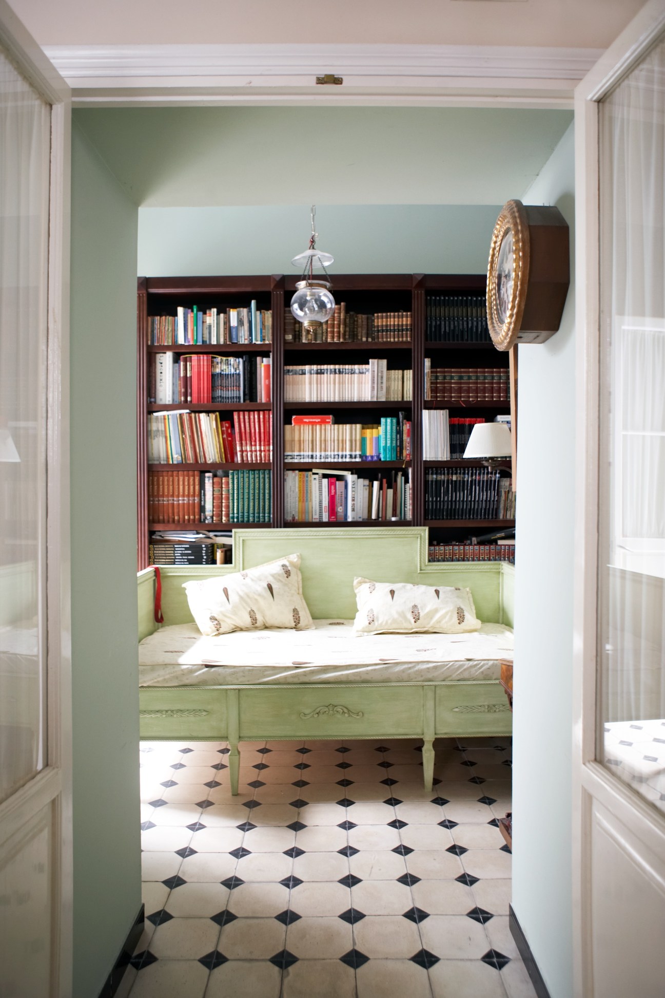 A bedroom alcove with green-painted bed frame, built-in bookshelves above, patterned floor tiles, and white doors opening to the space.