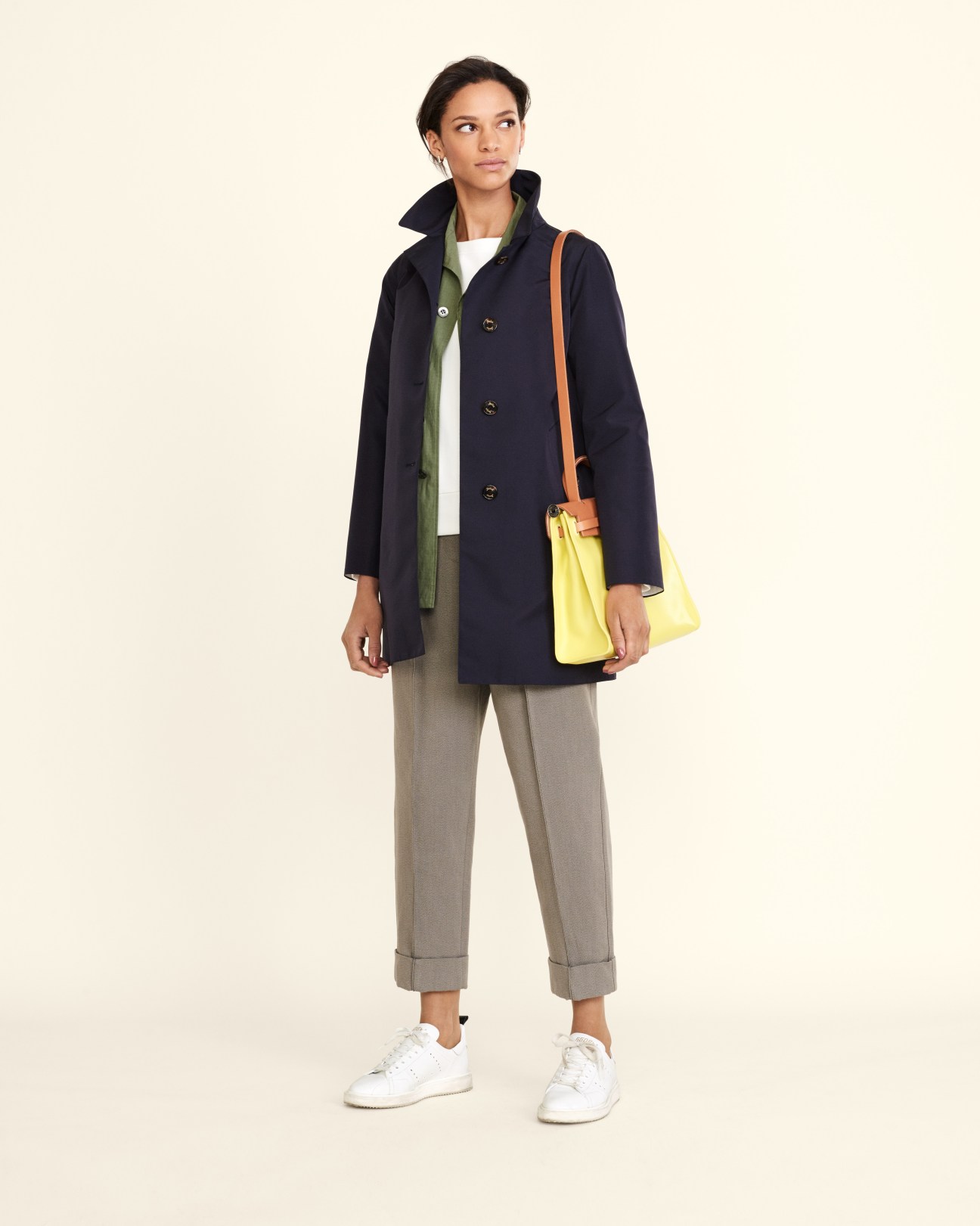 Woman wearing navy Sealup coat, Bottega Veneta trousers, white trainers and Hermès yellow bag.