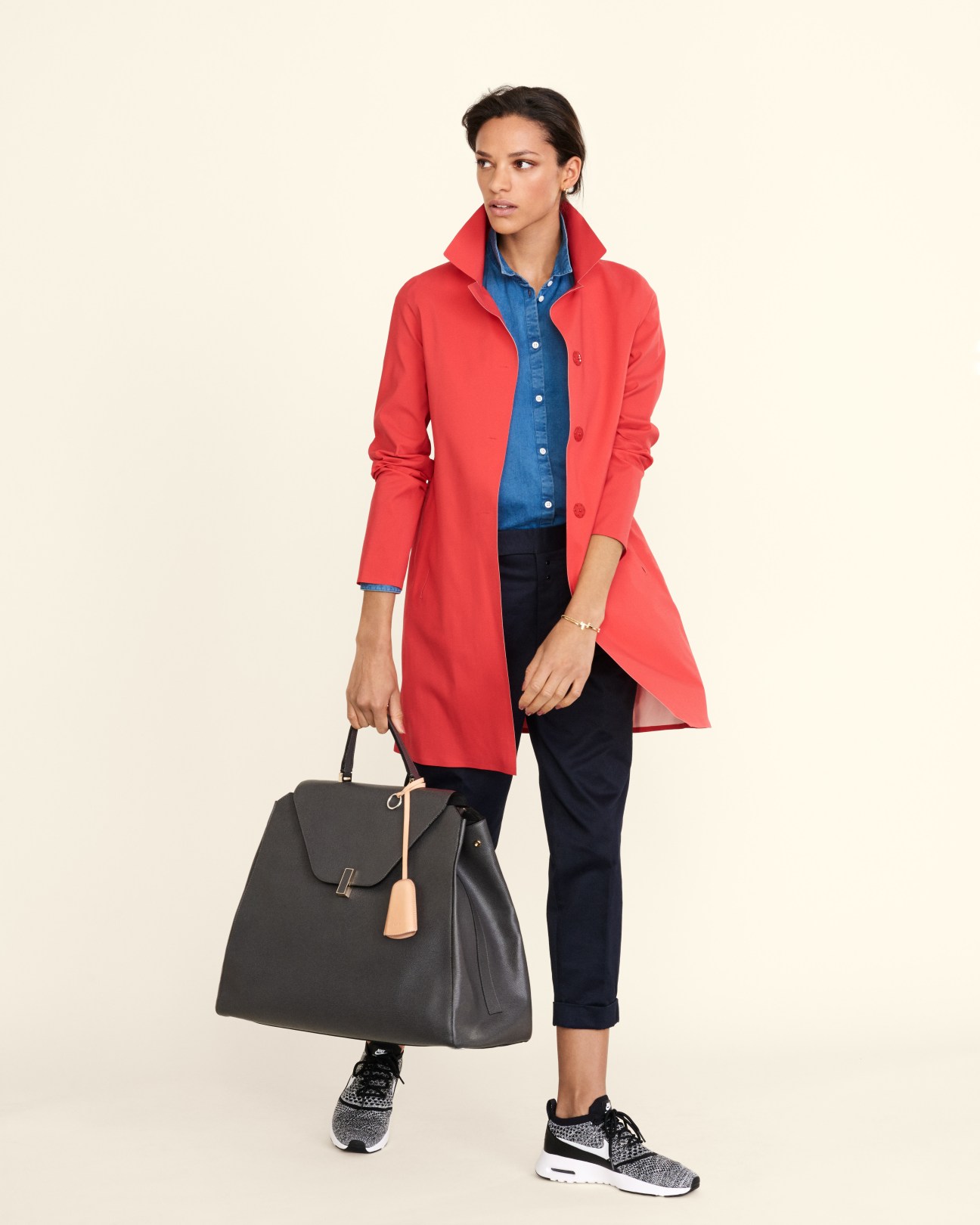 Woman wearing a red Herno coat, Norse Projects shirt, and Scye trousers with Nike trainers and Valextra bag.
