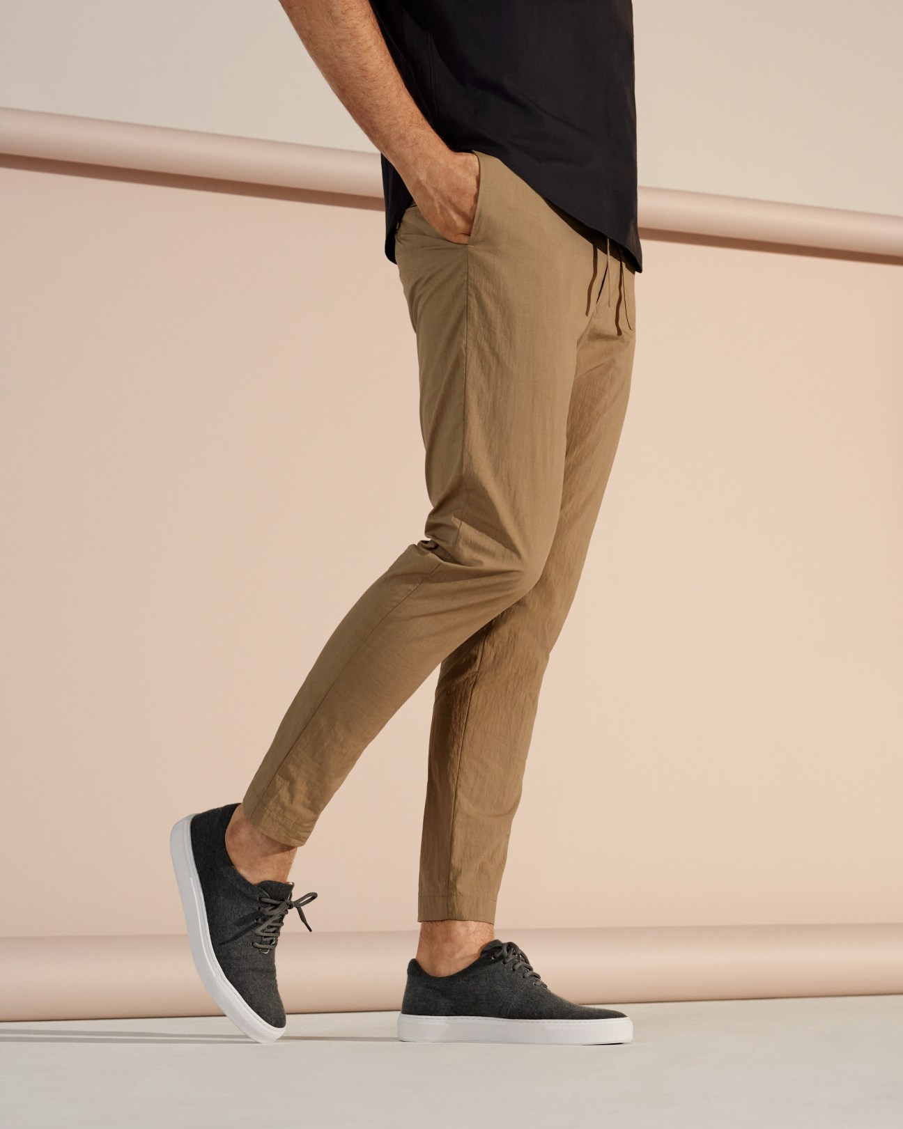 Man wearing beige trousers by Undecorated Man, black shirt and dark trainers by AMB.