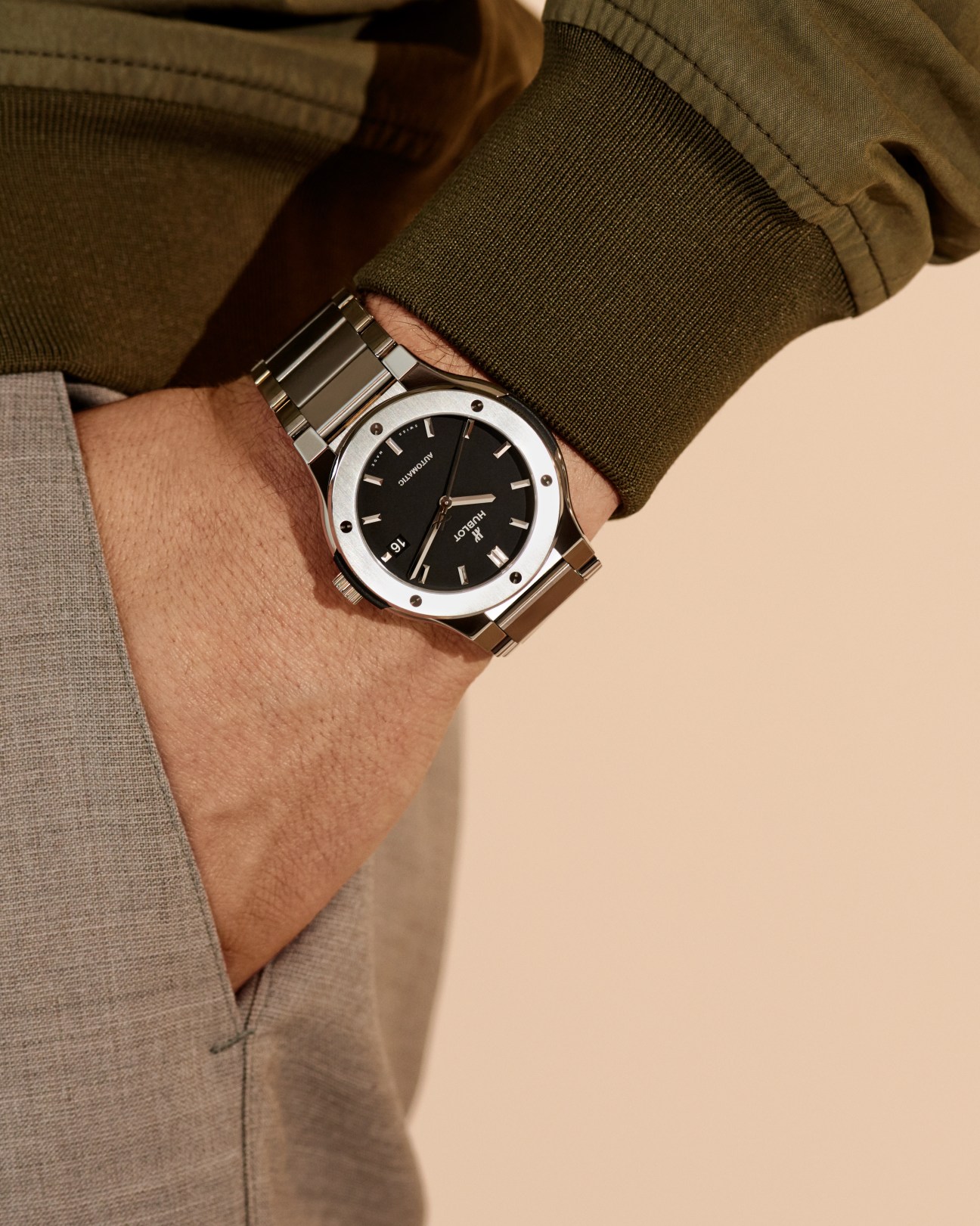 Man wearing olive cardigan and beige trousers with a Hublot watch on his wrist.