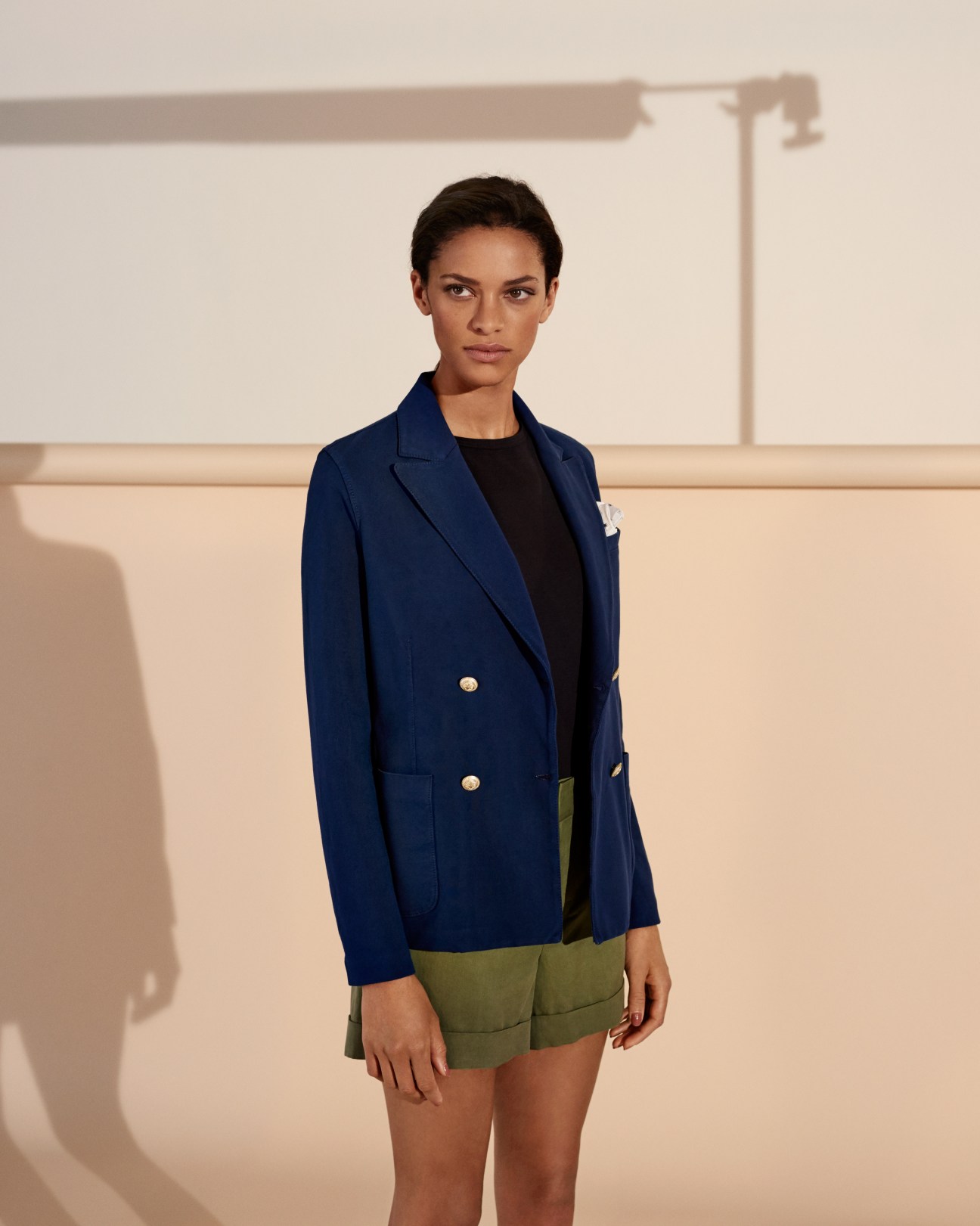 Model wearing navy blazer by Circolo 1901, black t-shirt by Sunspel, and olive shorts by Vince.