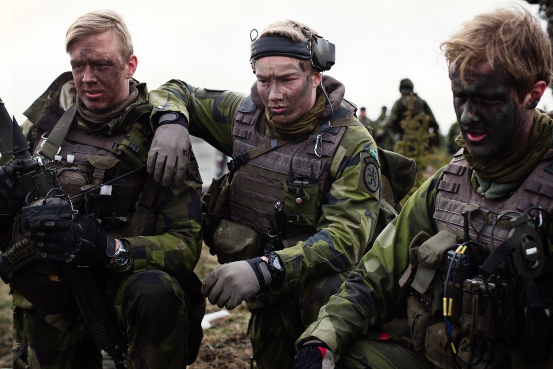 Swedish soldiers in military gear and tactical equipment debrief on an icy field after a training exercise.
