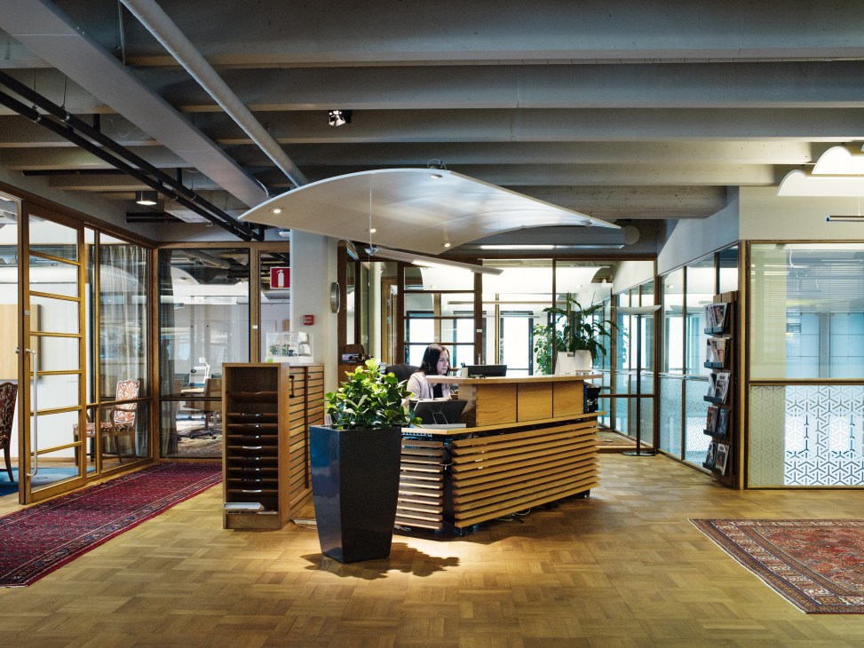 Modern office lobby with wooden reception desk, potted plants, and employees working at desk under curved ceiling in Scania headquarters.