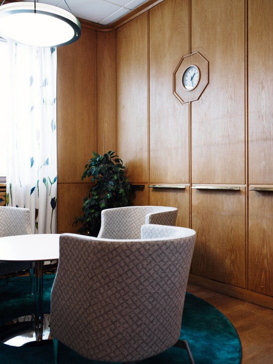 Mid-century modern office interior with oak wood paneling, curved upholstered chairs, and a round table.