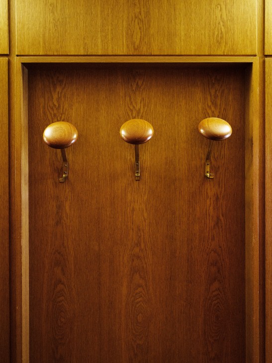 Three brass coat hooks on a wooden cabinet panel in Scania's office interior.