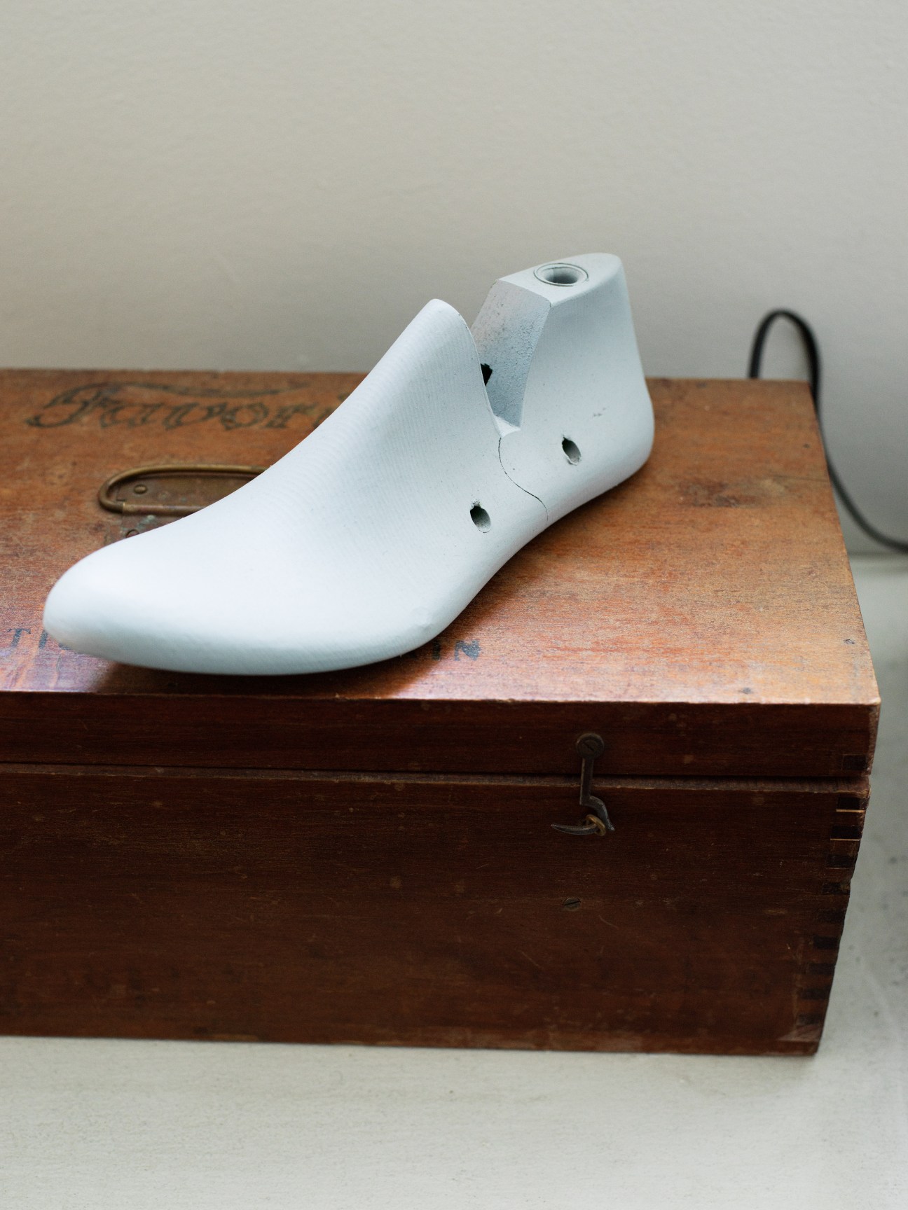 A white shoe last displayed on a vintage wooden box.