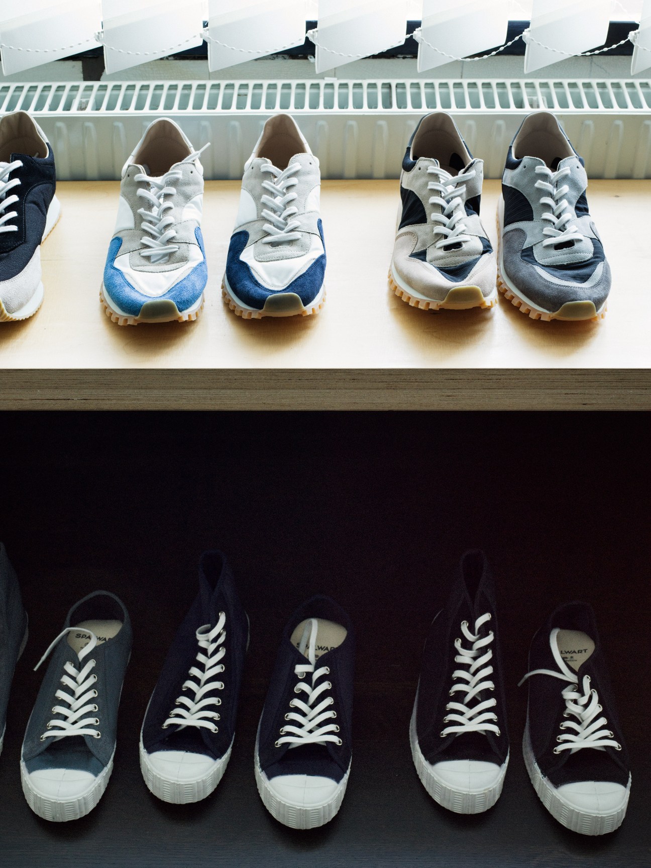 Spalwart sneakers displayed on shelves, including navy and white colorblock trainers above and navy canvas high-tops below.
