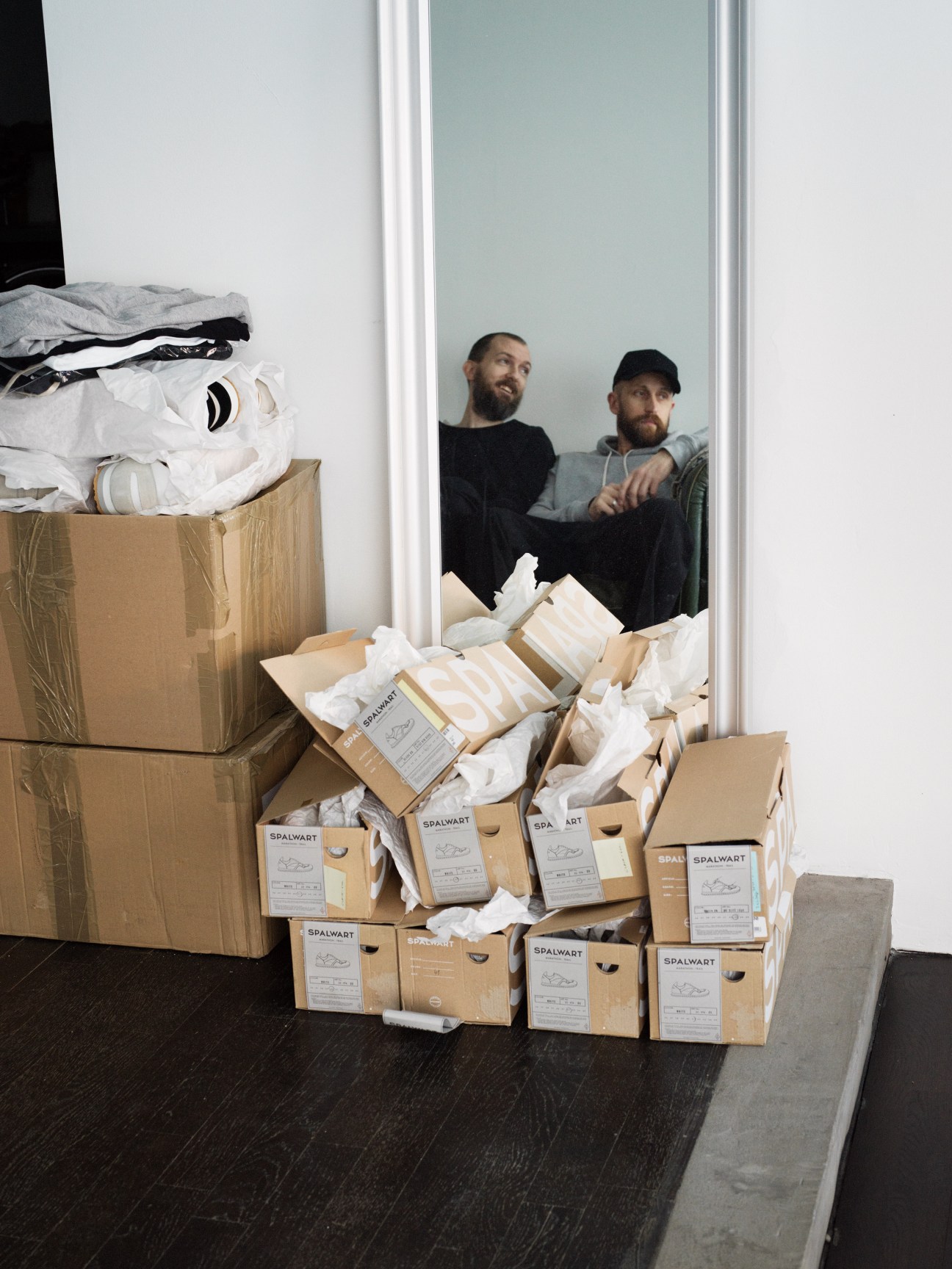Two men stand behind stacks of Spalwart shoe boxes made in Slovakia, with white tissue paper visible.