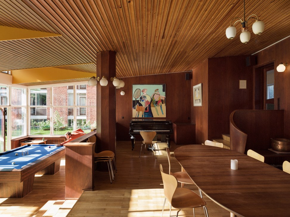 4th May College living room with wooden ceiling, pool table, piano, fireplace and large windows overlooking gardens.