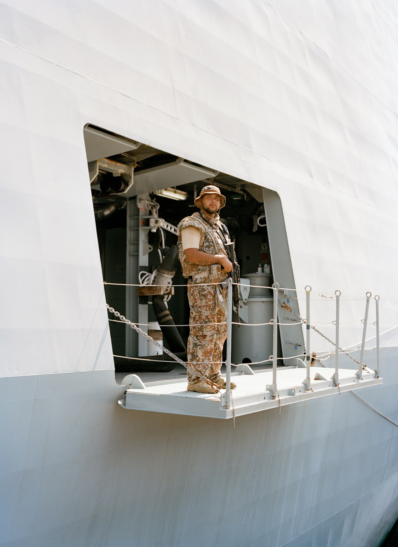 A Danish Navy sailor in desert camouflage uniform stands at an open hatch on HDMS Absalon.