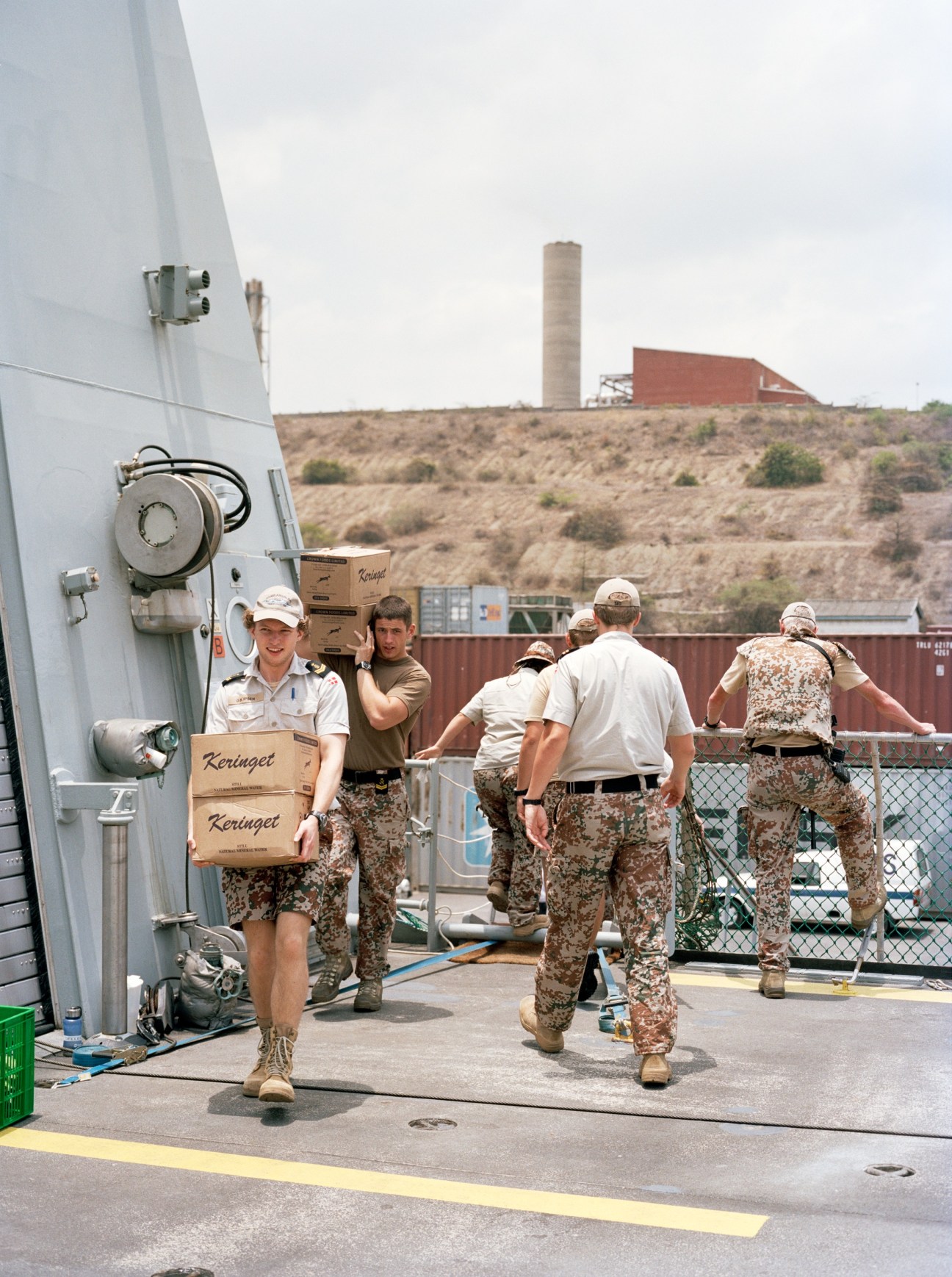Danish Navy crew members in camouflage uniforms loading cardboard boxes onto HDMS Absalon at port.