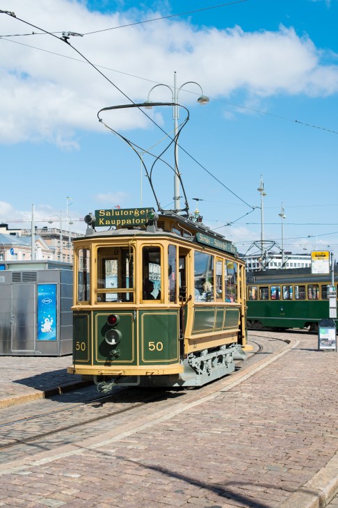 Yellow and green vintage tram number 50 on Helsinki street with overhead electric lines.