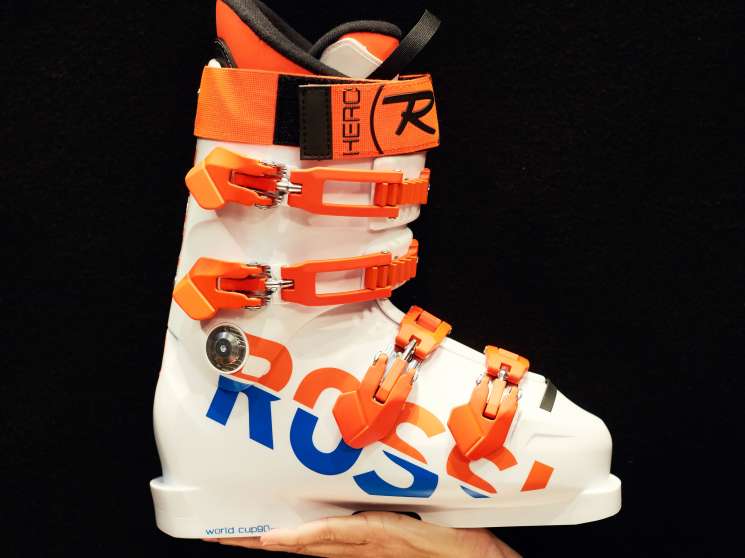 Rossignol Hero Wo Cup SI ZB ski boot with white shell and orange accents held in a hand against black background
