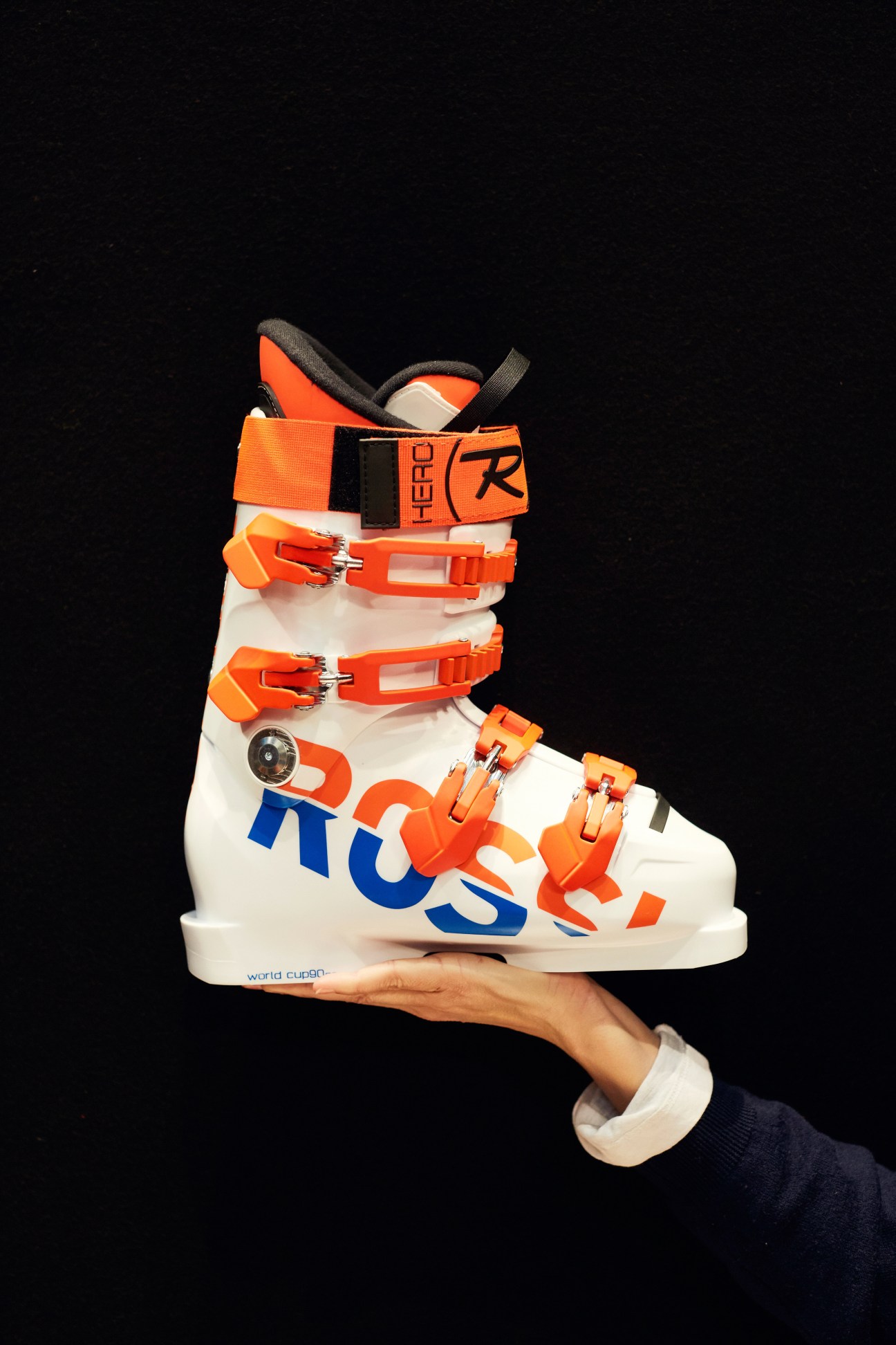 Rossignol Hero Wo Cup SI ZB ski boot with white shell and orange accents held in a hand against black background