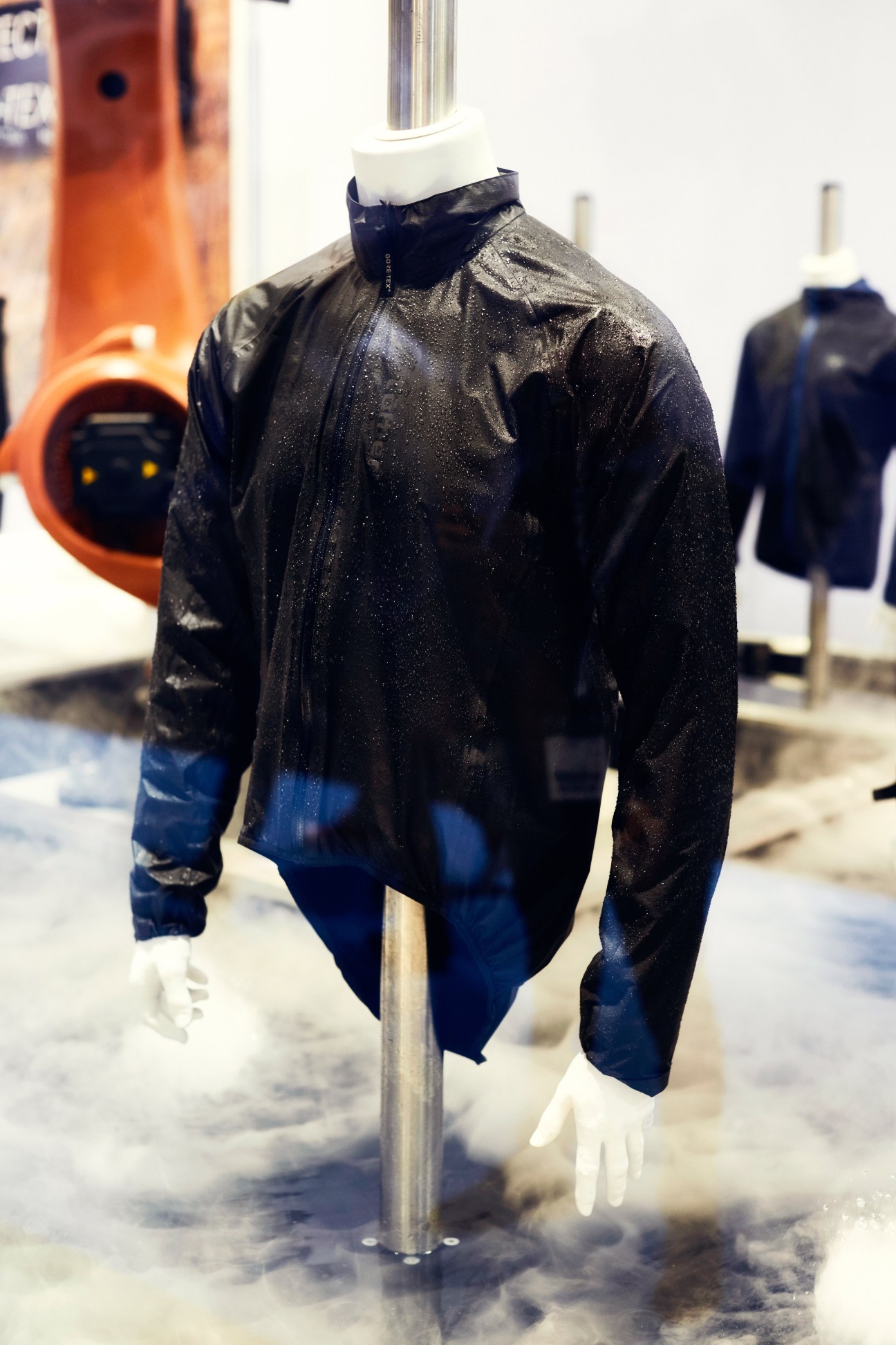 Gore-Tex testing machine spraying water on a black and blue jacket displayed on a mannequin.