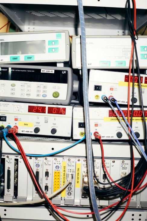 Close-up of electronic testing equipment and circuit boards with colorful wires and control panels in a laboratory setting.